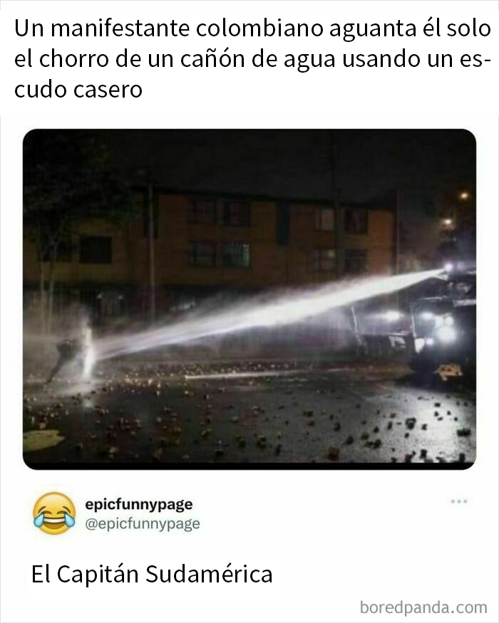 Manifestante colombiano resiste un cañón de agua con un escudo casero en una calle, escena caótica y divertida.