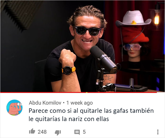 Hombre con gafas negras sonriendo frente a un micrófono en un estudio grabando contenido sobre insultos geniales.