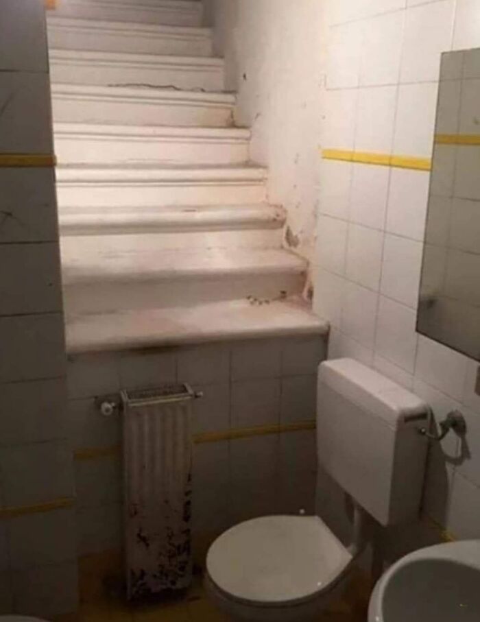 Escalera instalada dentro de un baño pequeño con inodoro y radiator viejo, ejemplo de personas que menos mal que hicieron una foto.