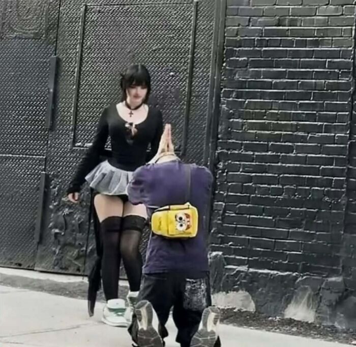 Persona arrodillada con mochila amarilla frente a mujer vestida con falda gris y medias negras, escena que provoca mucha vergüenza ajena.
