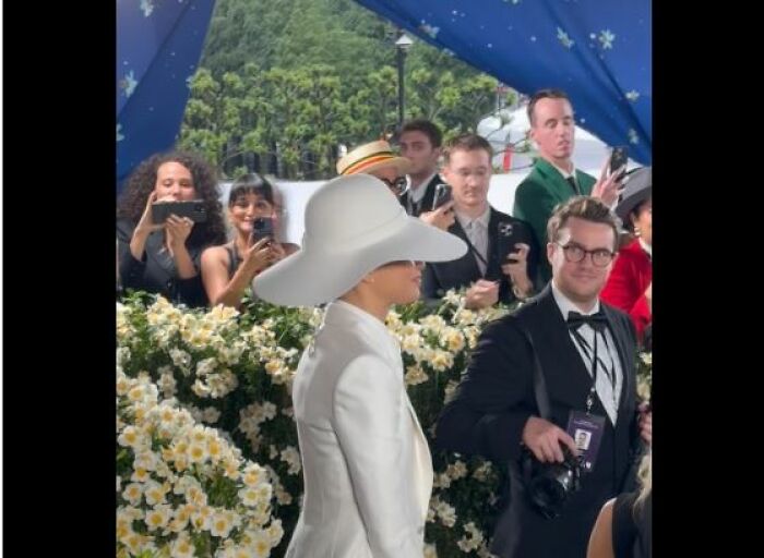 Persona con sombrero blanco grande en la alfombra roja, rodeada de fotógrafos, momentos incómodos en la Gala Met 2025.