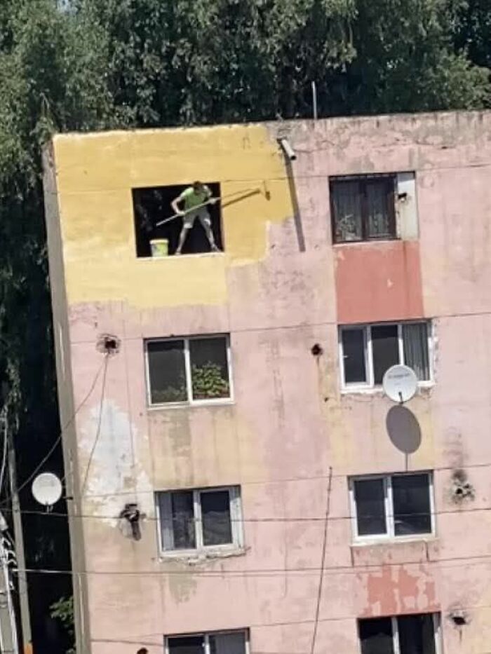 Persona pintando fachada en edificio, fotografía que muestra un momento único y difícil de creer.