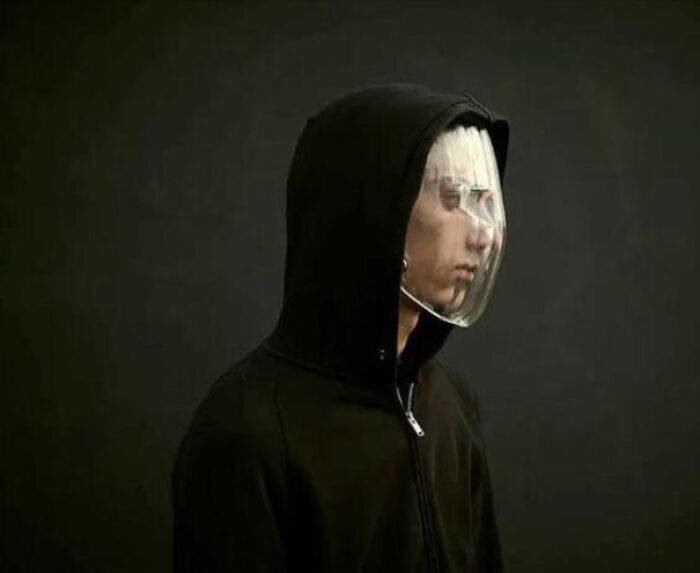 Persona con sudadera negra y capucha usando una máscara facial plástica transparente, imagen interesante y curiosa encontrada.