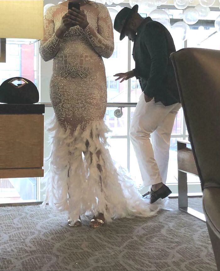 Novia con vestido de plumas y perlas junto a novio con sombrero en evento, destacando peores vestidos y atuendos de boda.