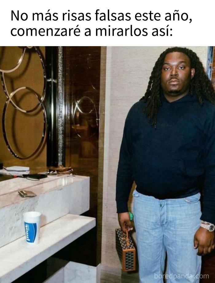 Hombre serio con sudadera y jeans, sosteniendo bolso, meme absurdo de performance art borderline en interior moderno.