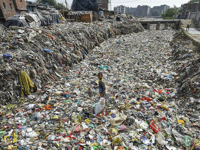 Un niño recoge artículos reciclables de un desagüe semiseco, en Taimoor Nagar, Nueva Delhi