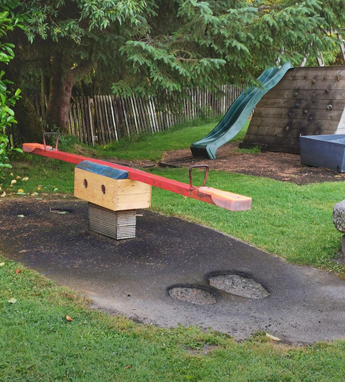 Un subibaja en mi parque infantil local donde miles de pies pequeños han desgastado el asfalto hasta atravesarlo