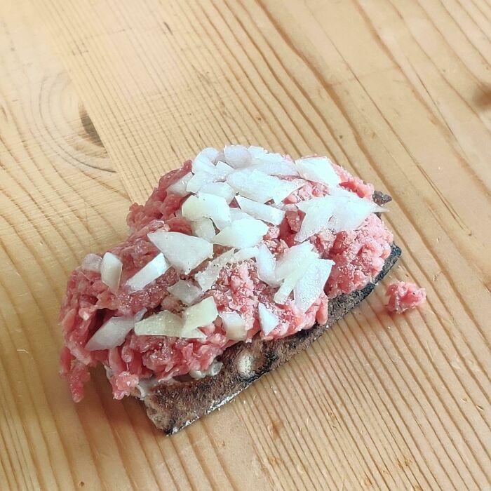 El sándwich que le gusta comer a mi padre, carne picada cruda con cebolla cruda y pimienta blanca sobre pan duro
