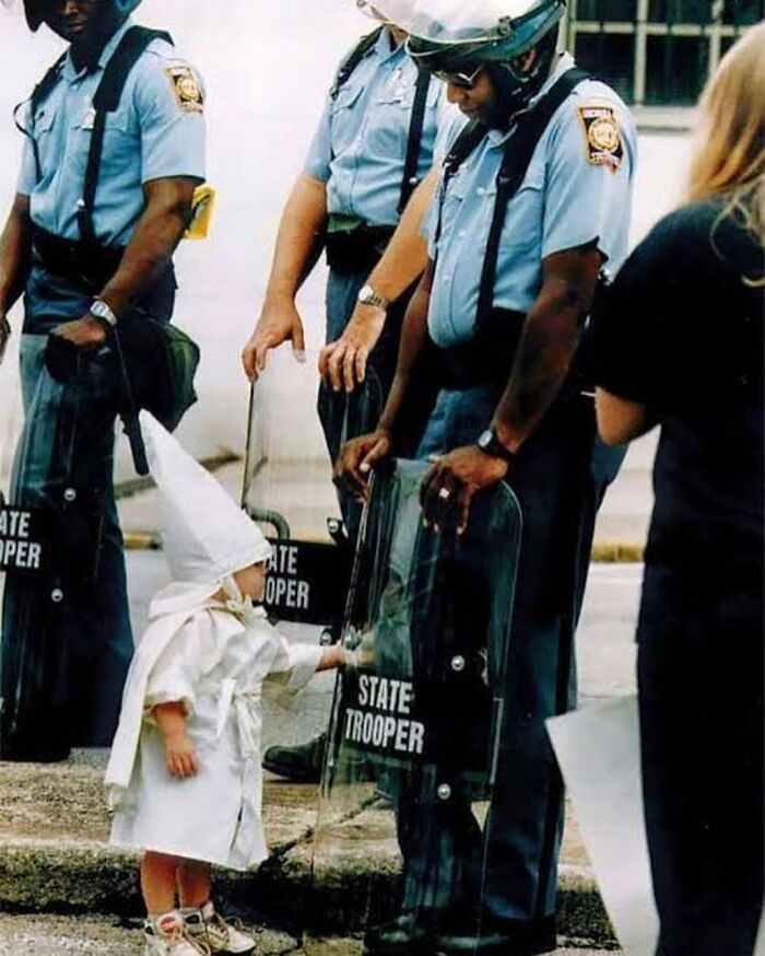 Fotografía de Todd Robertson: "Nadie nace racista". Un niño vestido con una túnica y una capucha del KKK, toca curiosamente el escudo de un policía estatal durante un mitin del KKK en Gainesville, Georgia, 1992