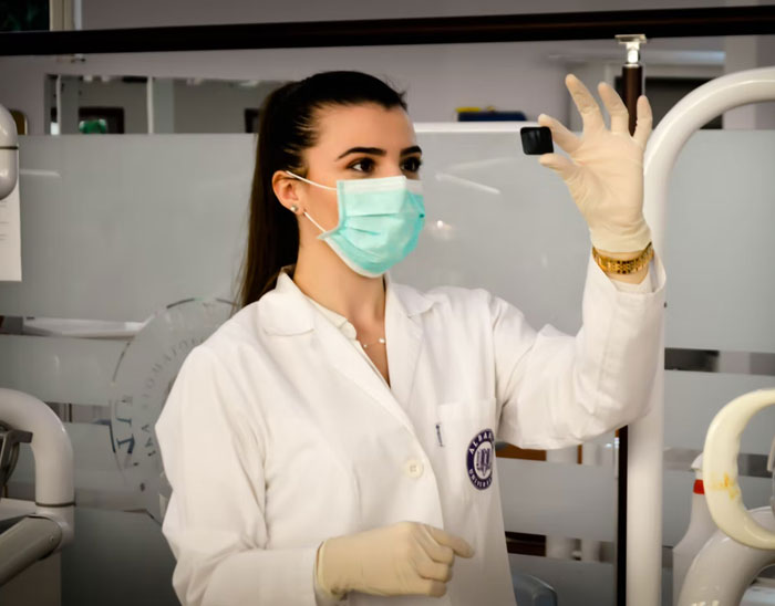 Mujer con bata y mascarilla en clínica dental, examinando pieza negra pequeña, datos muy informativos en salud.