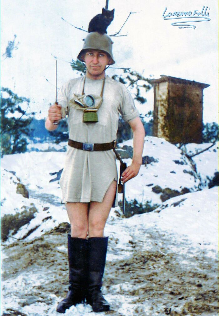 Una divertida fotografía de la Primera Guerra Mundial, soldado alemán en la nieve llevando sólo un casco, botas y una camiseta con un gato en la cabeza. 1916