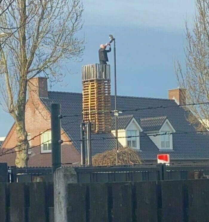 Es solo un hombre sobre una pila de tarimas levantadas por una carretilla elevadora cambiando el foco de un farol
