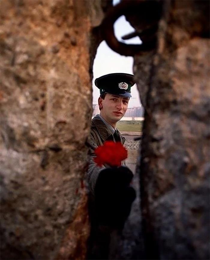 Un guardia fronterizo de Alemania Oriental ofrece una flor a través de un hueco en el Muro de Berlín la mañana de su caída, 1989