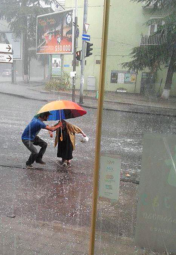 Un joven protege a una anciana del granizo mientras cruza la carretera. Tbilisi, Georgia