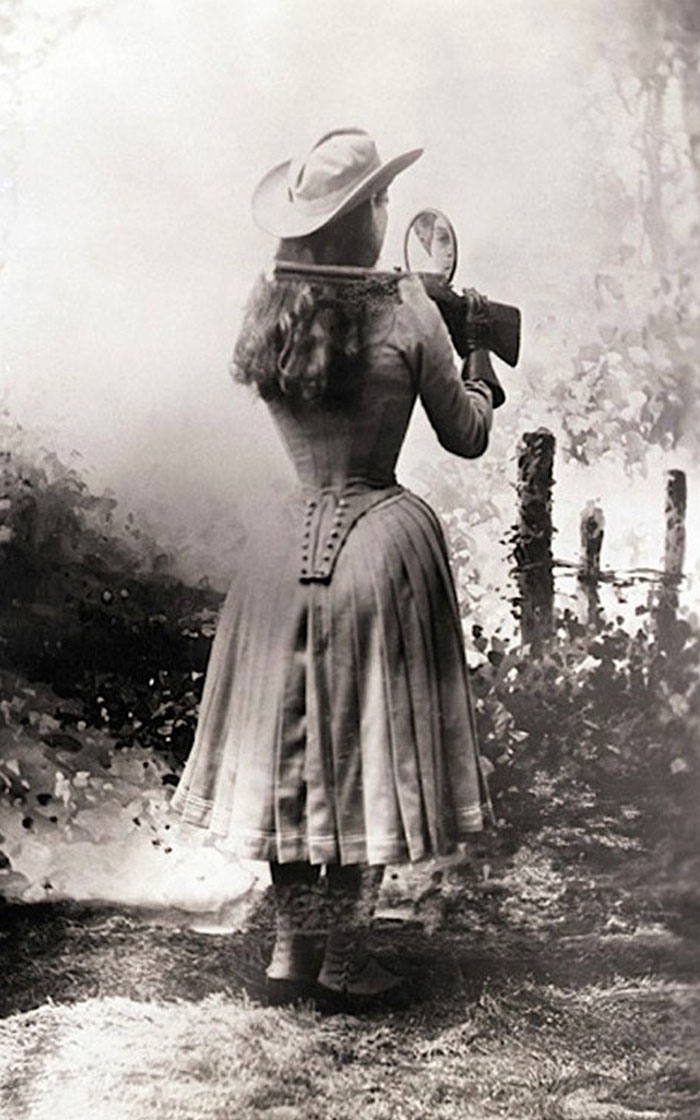 Annie Oakley disparando un arma por encima del hombro con un espejo de mano, 1899