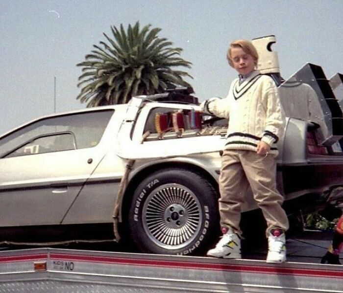Macaulay Culkin con zapatillas Reebok apoyado en el Delorean