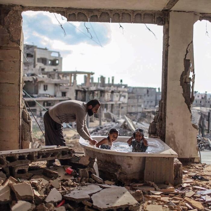Padre bañando a su hija y a su sobrina en su casa bombardeada en Gaza, 2015, por @emadsnassar