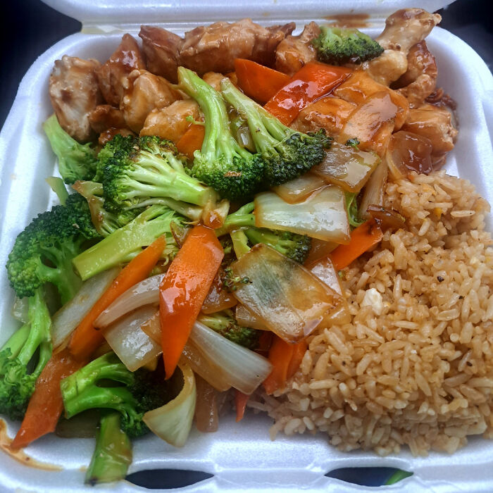 Plato de comida para llevar con pollo teriyaki, arroz frito y vegetales salteados, personas felices por su pedido exacto.