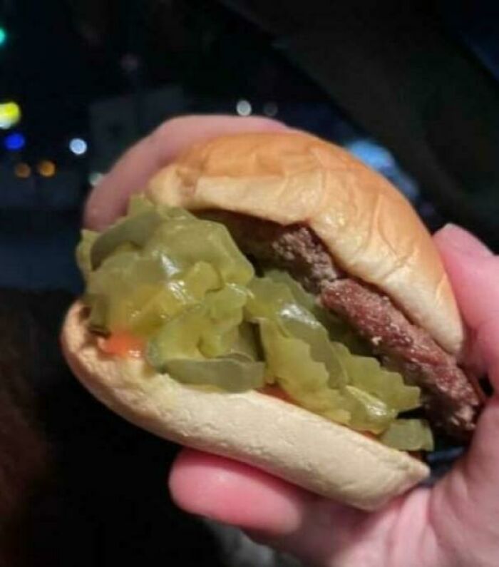 Persona sosteniendo una hamburguesa con pepinillos, ejemplo de personas que se alegran al recibir exactamente su pedido