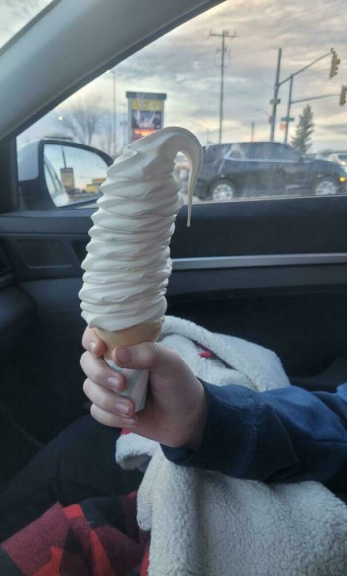 Helado de vainilla gigante en cucurucho sostenido por una persona feliz en un coche, ejemplo de pedido exacto recibido.