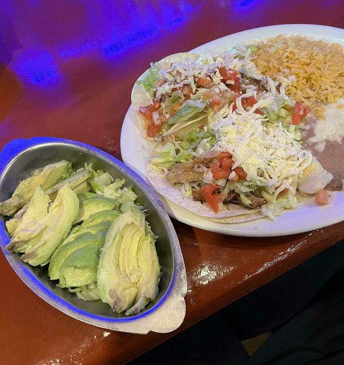 Tacos con carne, queso, lechuga y tomate, acompañados de arroz, frijoles y aguacate frescos en plato y recipiente metálico.