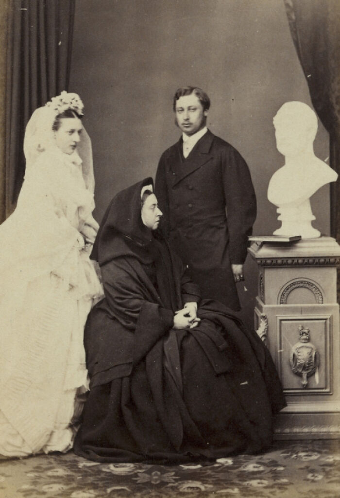 Tres personas frente a un busto en una boda antigua.