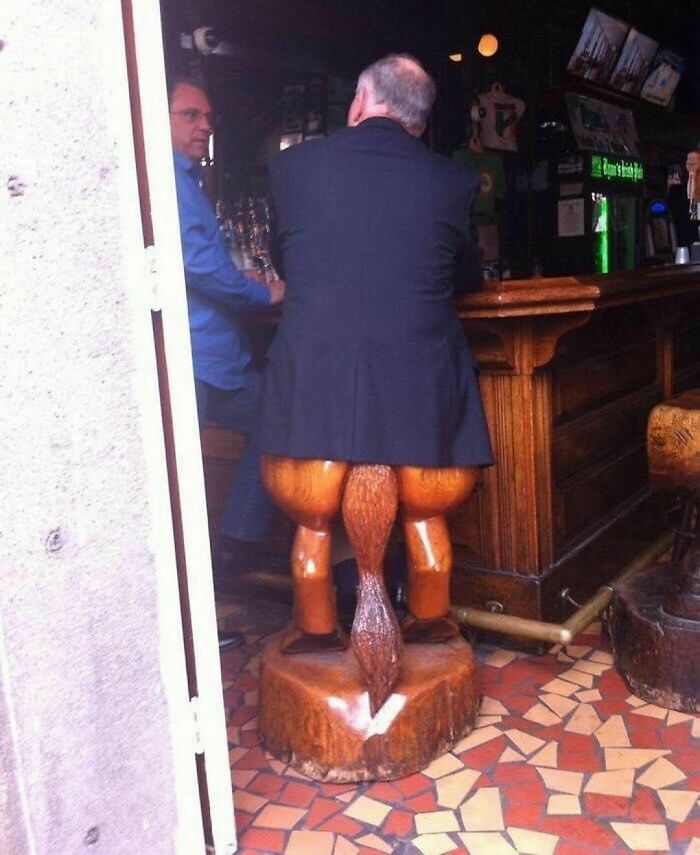 Hombre sentado en taburete con patas y cola de madera en un bar, imagen que resulta horrible pero divertida y incómoda.
