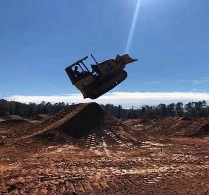 Máquina pesada en salto extremo sobre montículo de tierra, imagen realmente incómoda y divertida en construcción.