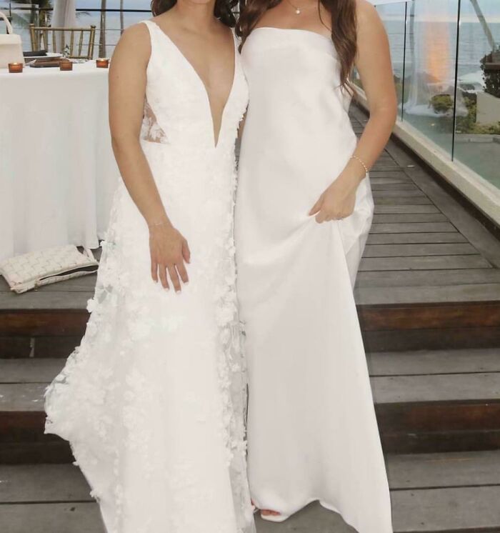 Dos mujeres en vestidos de boda blancos, posando en una terraza con vistas al mar. Bodas vergonzosas en internet.