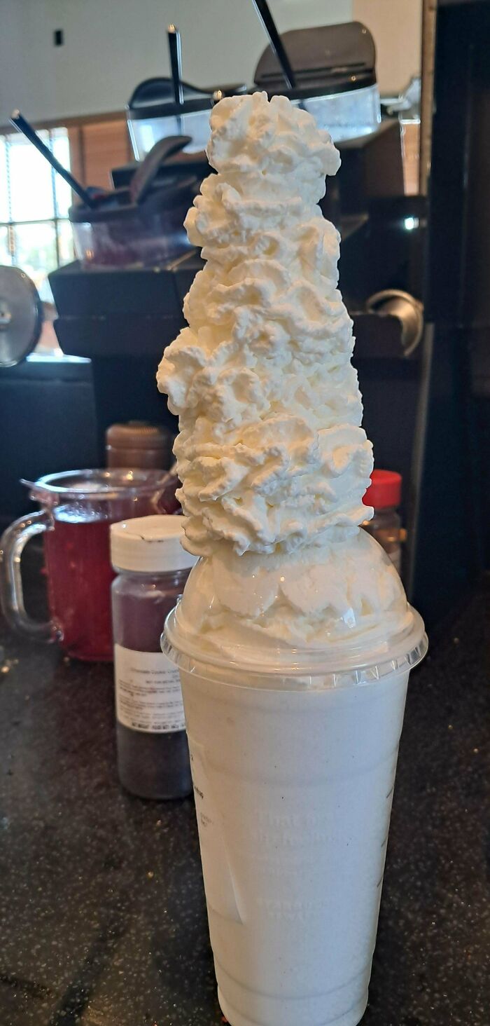 Vaso con batido blanco y una enorme cantidad de crema batida, mostrando una felicidad al recibir exactamente eso pedido.