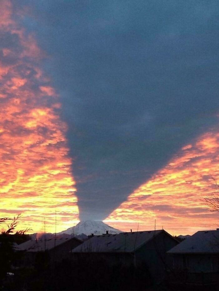 Sombra gigante y aterradora proyectada desde una montaña al atardecer con cielo colorido y nubes.