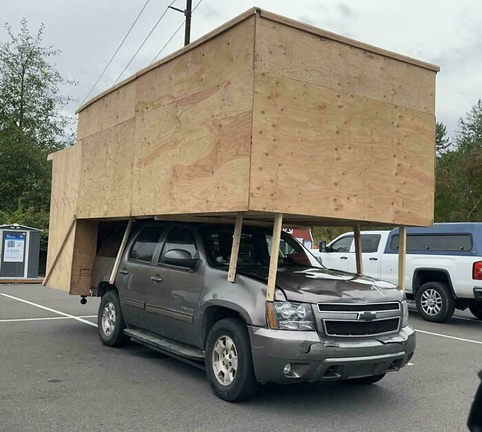 Vehículo con proyecto casero fallido, estructura de madera mal instalada que afecta la funcionalidad del auto en el estacionamiento.