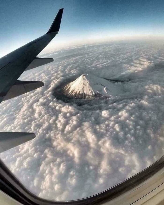 Vista aérea desde un avión de una montaña nevada emergiendo entre grandes nubes, mostrando objetos extremadamente grandes y aterradores.