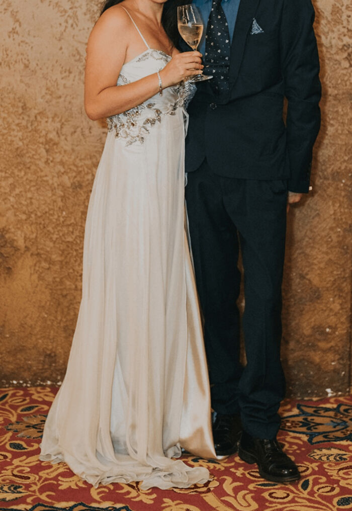 Pareja vestida elegante en una boda vergonzosa, ella con copa de vino y vestido blanco, él con traje oscuro.