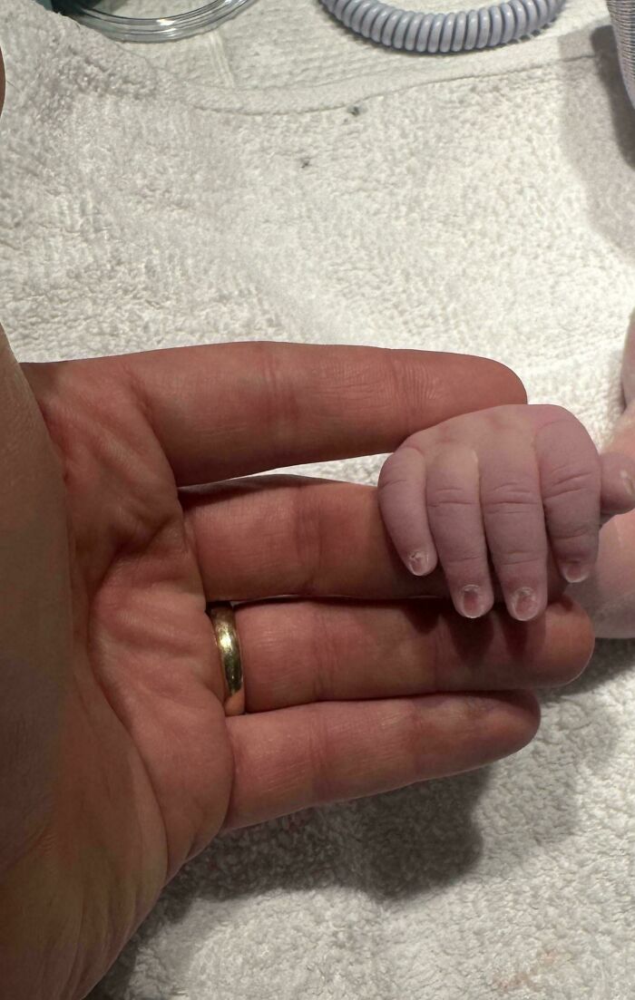 Mano de padre con anillo de boda sosteniendo la pequeña mano de un bebé, momento tierno de paternidad.