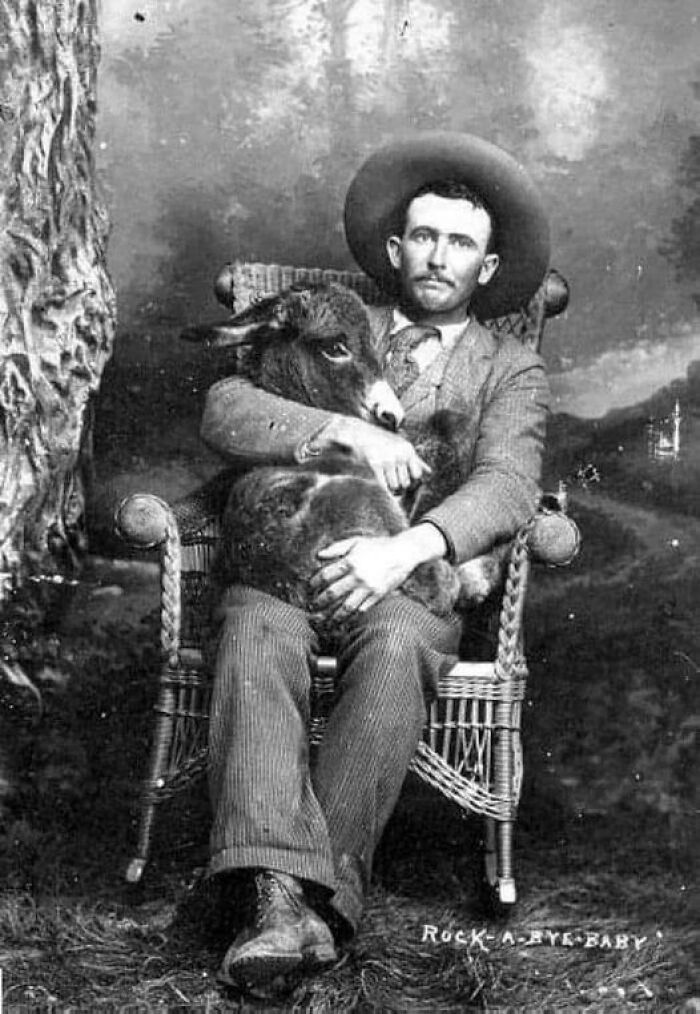 Un hombre posa con un burro en el regazo, década de 1910