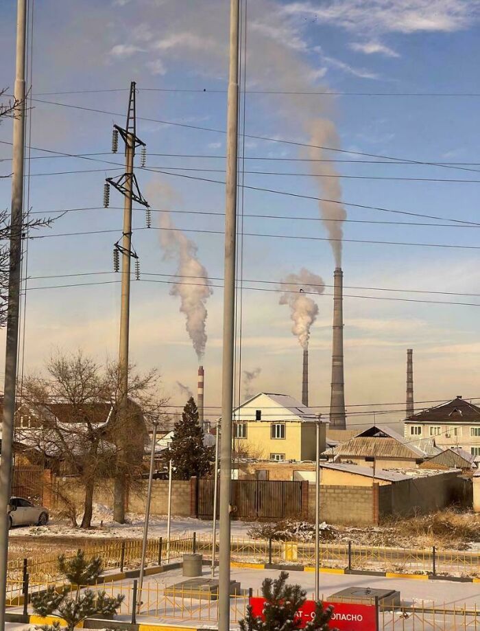 Chimeneas industriales emitiendo humo sobre un área residencial, representando un infierno urbano moderno.