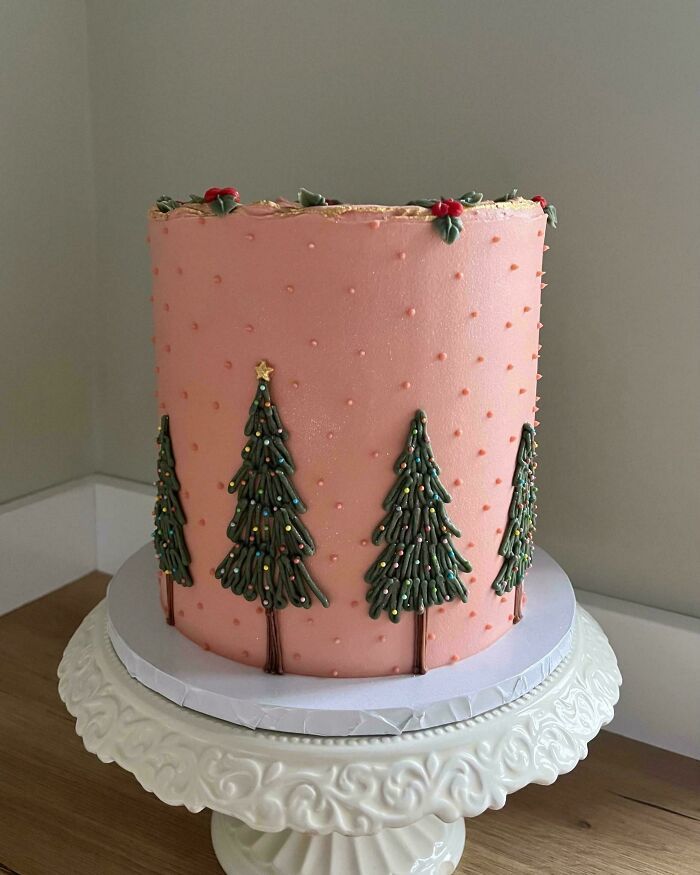 Pastel de repostería decorado con árboles navideños en glaseado verde sobre fondo rosa en expositor blanco.