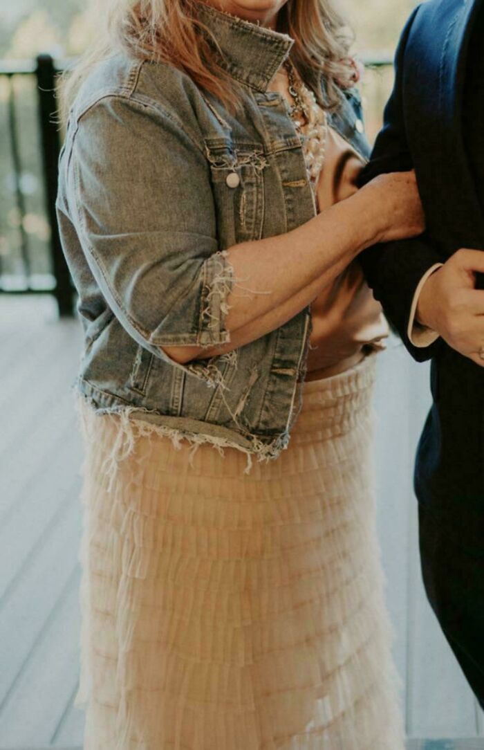 Persona en boda con chaqueta de mezclilla deshilachada y vestido de volantes, escena casual.