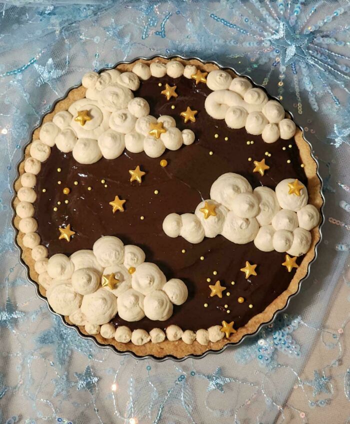 Tarta de repostería creativa con decoración de nubes y estrellas doradas sobre crema de chocolate, elevaron la repostería a otro nivel.