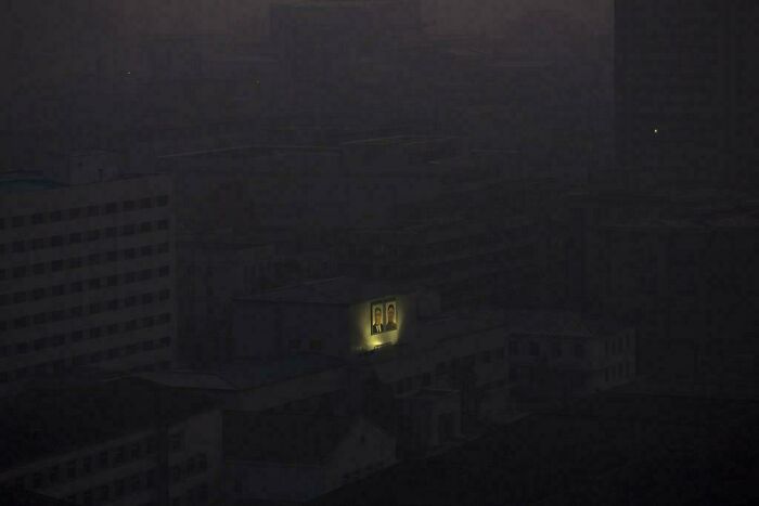 Edificio oscuro en infierno urbano con una luz destacando un retrato iluminado en la fachada.