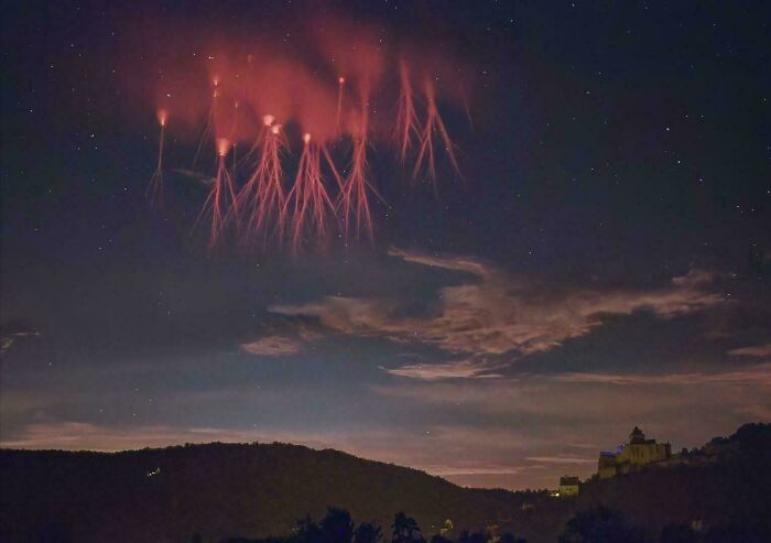 Luces rojas en el cielo nocturno, creando una escena extrañamente aterradora sobre el paisaje oscuro.