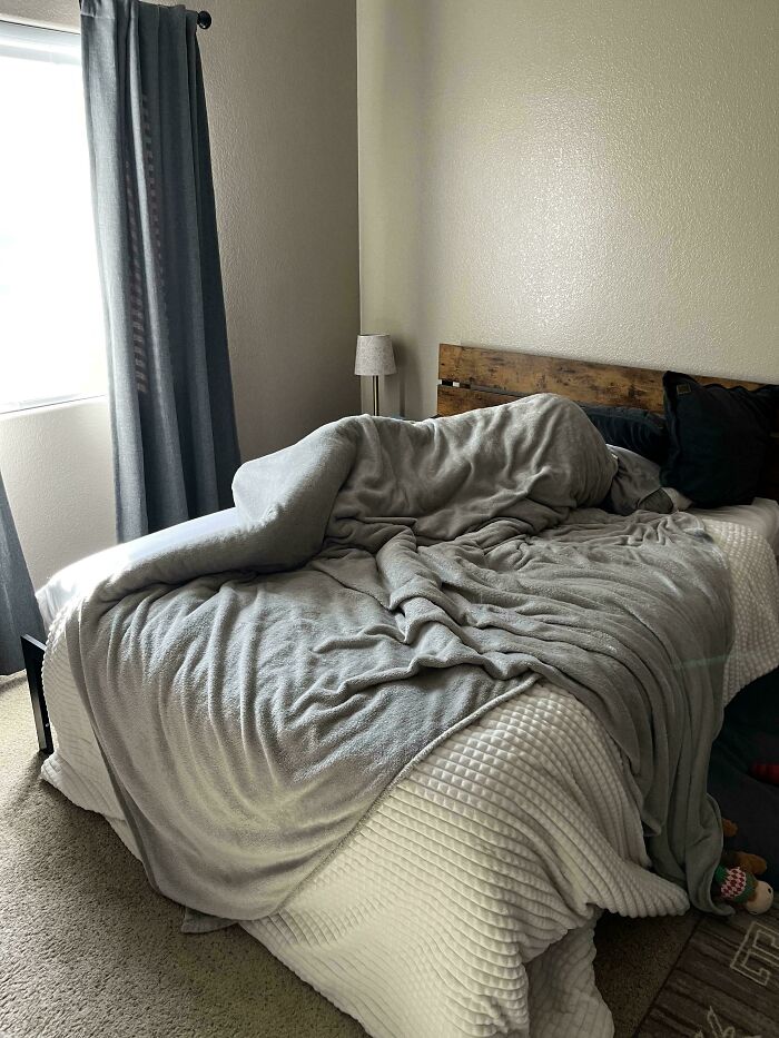 Cama con manta formando una figura humana, creando una escena extrañamente aterradora en una habitación iluminada.