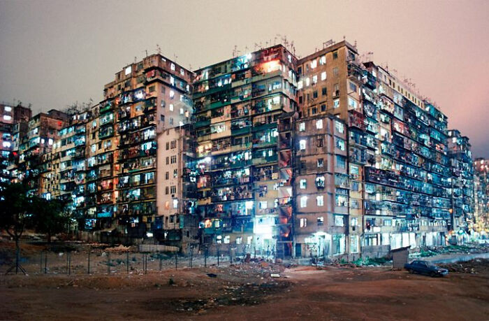 Edificio densamente poblado iluminado de noche, reflejando el infierno urbano construido por humanos.