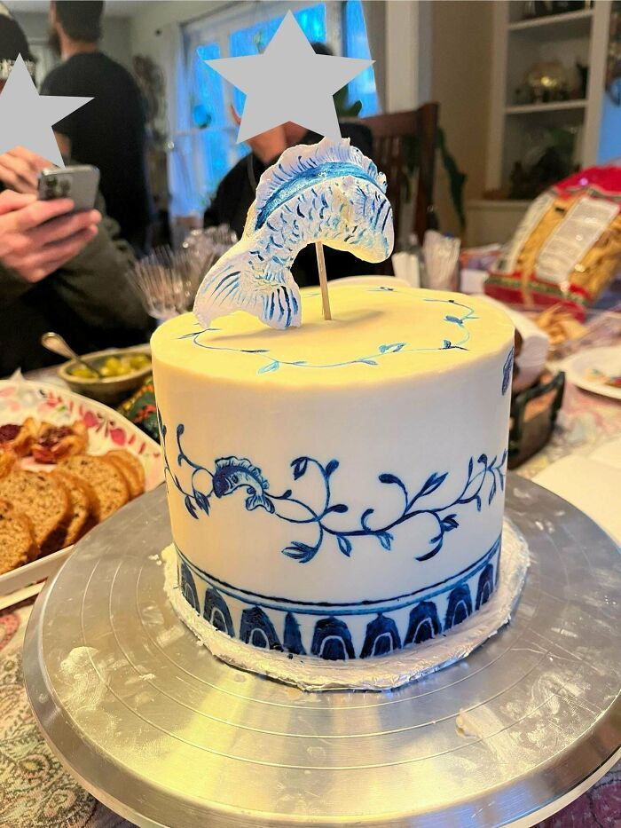 Pastel blanco decorado con detalles azules finos y una figura de pez en la parte superior, mostrando repostería creativa.