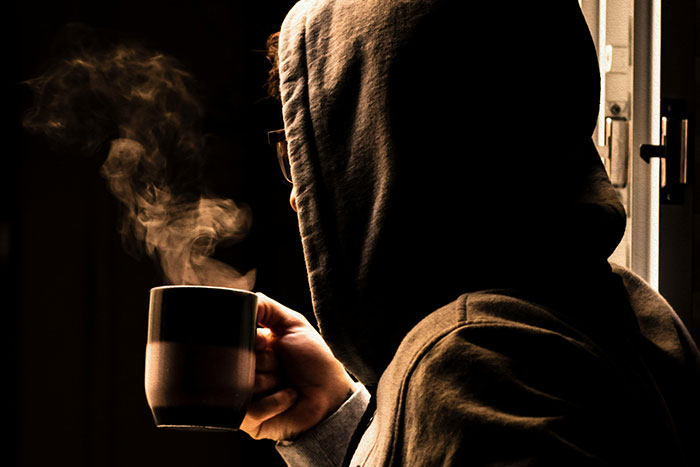 Persona con sudadera y gafas, tomando una taza humeante, representando códigos de trucos para el juego de la vida.