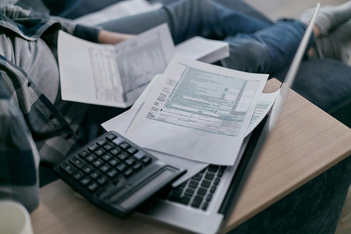 Persona revisando documentos y calculadora sobre una laptop, aplicando códigos de trucos para el juego de la vida.