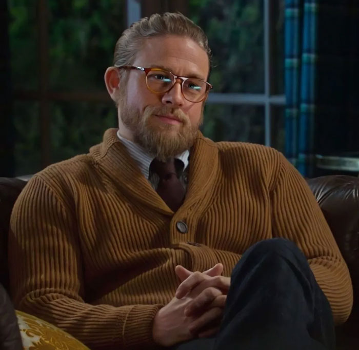 Hombre con gafas y suéter marrón sentado en sofá en interior, imagen relacionada con celebridades que se desvanecieron.