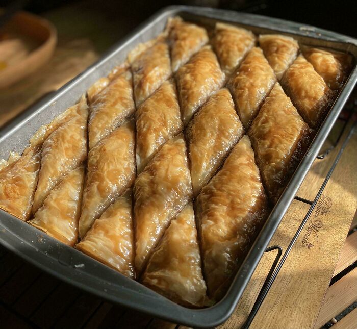 Repostería con baklava casero recién horneado en bandeja metálica mostrando textura crujiente y dorada al nivel profesional.