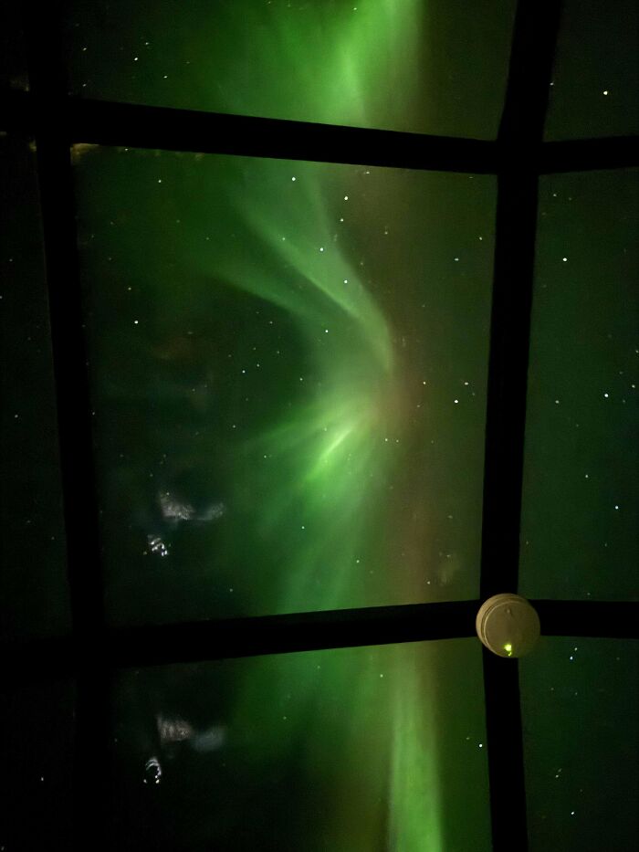 Aurora boreal verde vista a través de una ventana negra con un toque de surrealismo y estrellas en el cielo nocturno.
